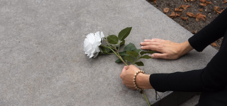 La Commemorazione dei Defunti: memoria, fede e responsabilità dei vivi una mano con un fiore in mano tocca una tomba